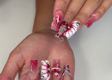 Diseño de uñas detallado en Nailsbycaprii, Avilés, ES con detalles rojos y blancos y adornos metálicos.