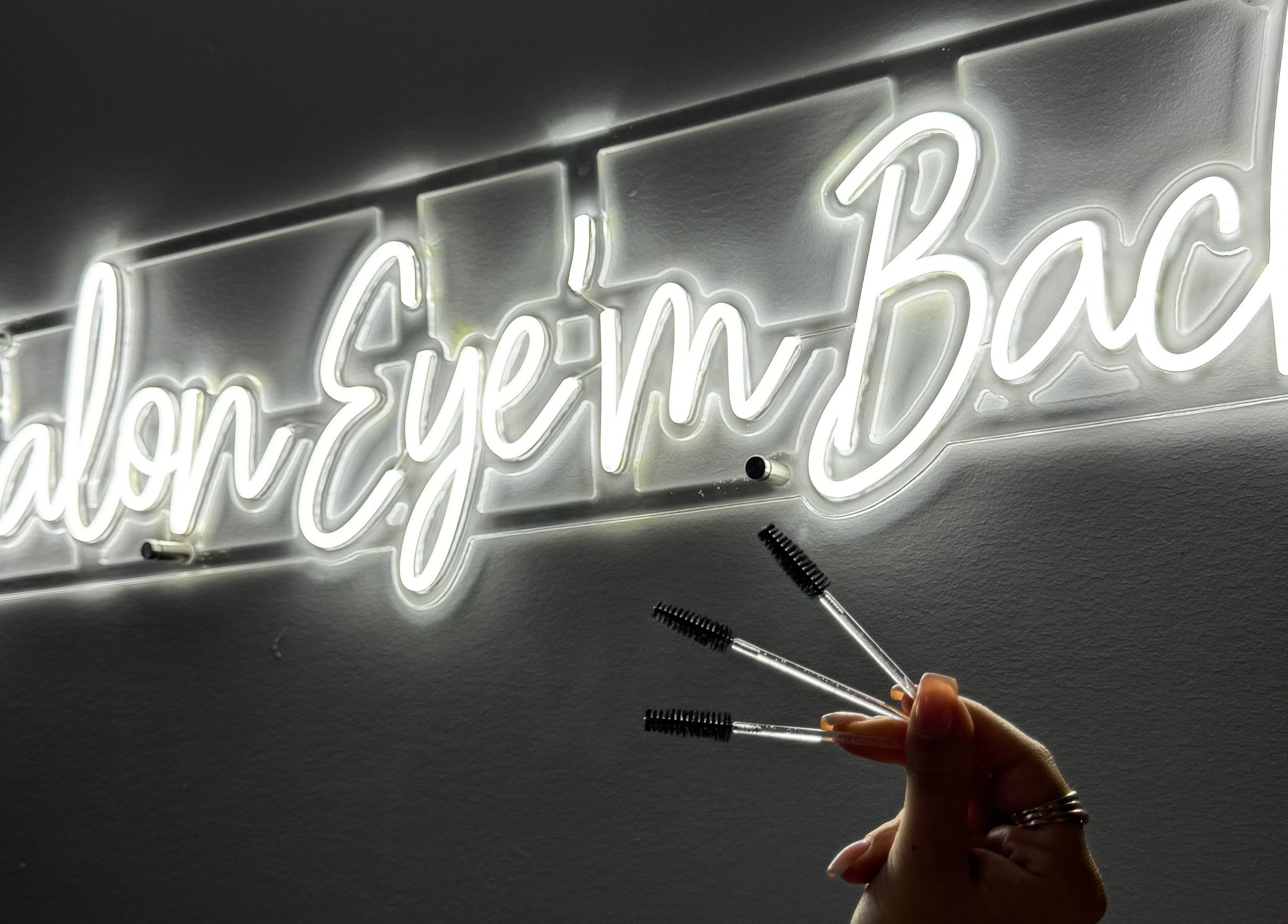 Enseigne néon de Salon Eye’m Back à Laval, Québec, CA, avec brosses à cils en main.