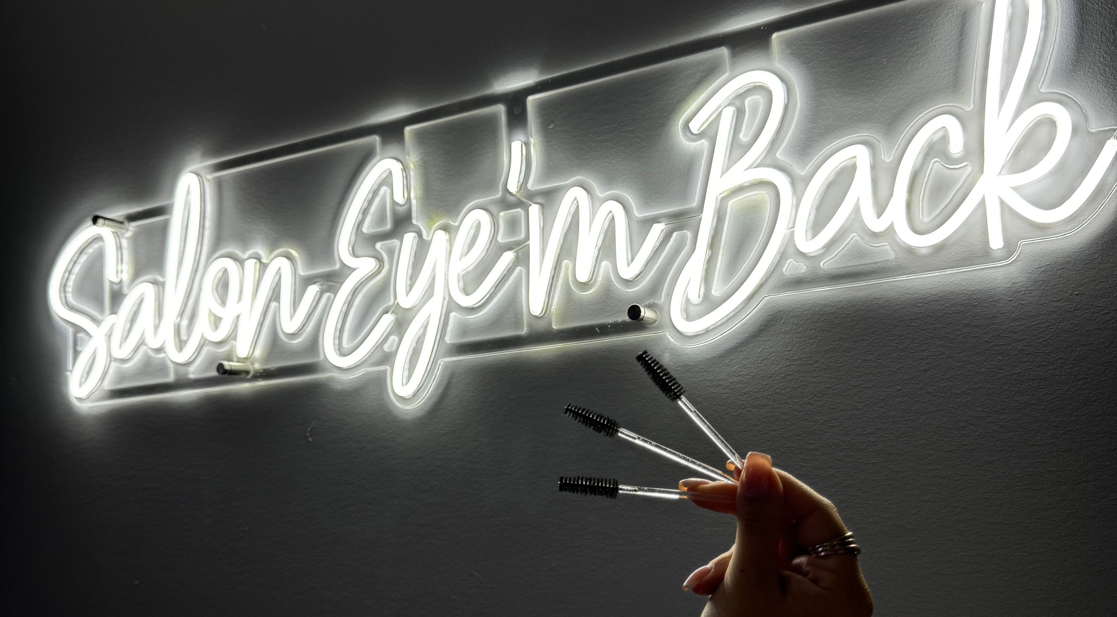 Enseigne néon de Salon Eye’m Back à Laval, Québec, CA, avec brosses à cils en main.