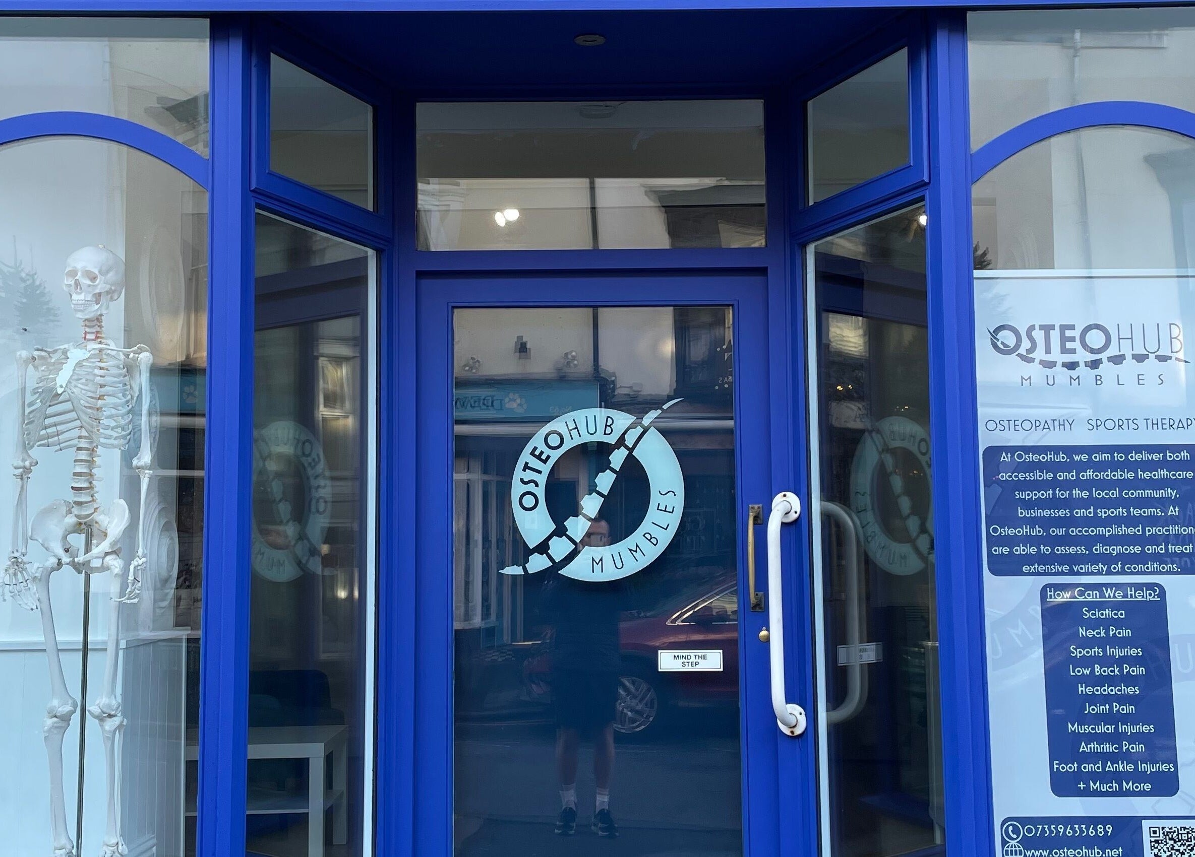 Front entrance of OsteoHub Mumbles in Swansea, Wales, GB with a skeleton display inside the blue-framed windows.