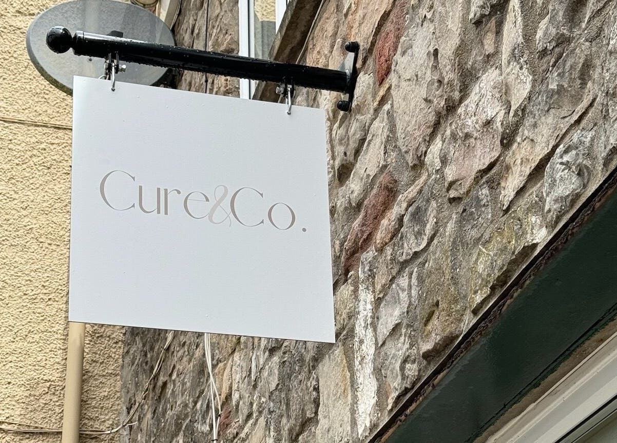 Cure&Co. signage mounted on a rustic stone wall in Chepstow, GB.