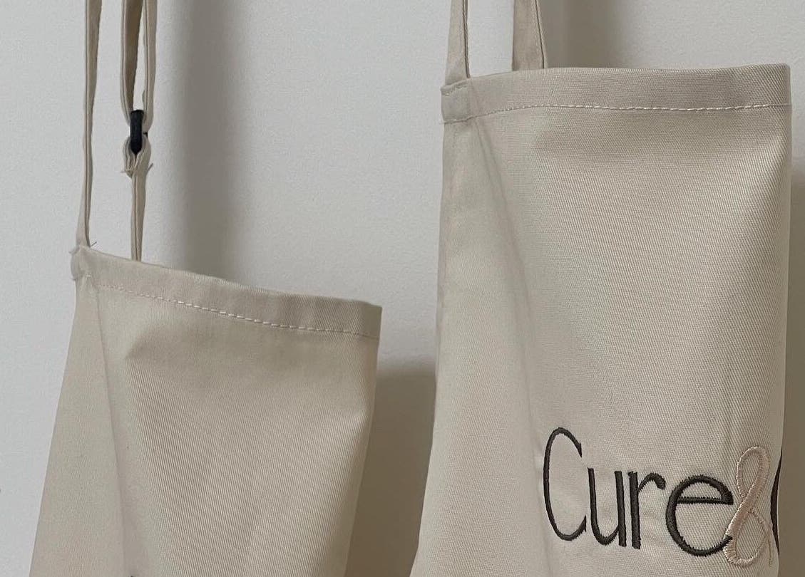 Cure&Co. branded tote bags hanging on a white wall in Chepstow, GB.