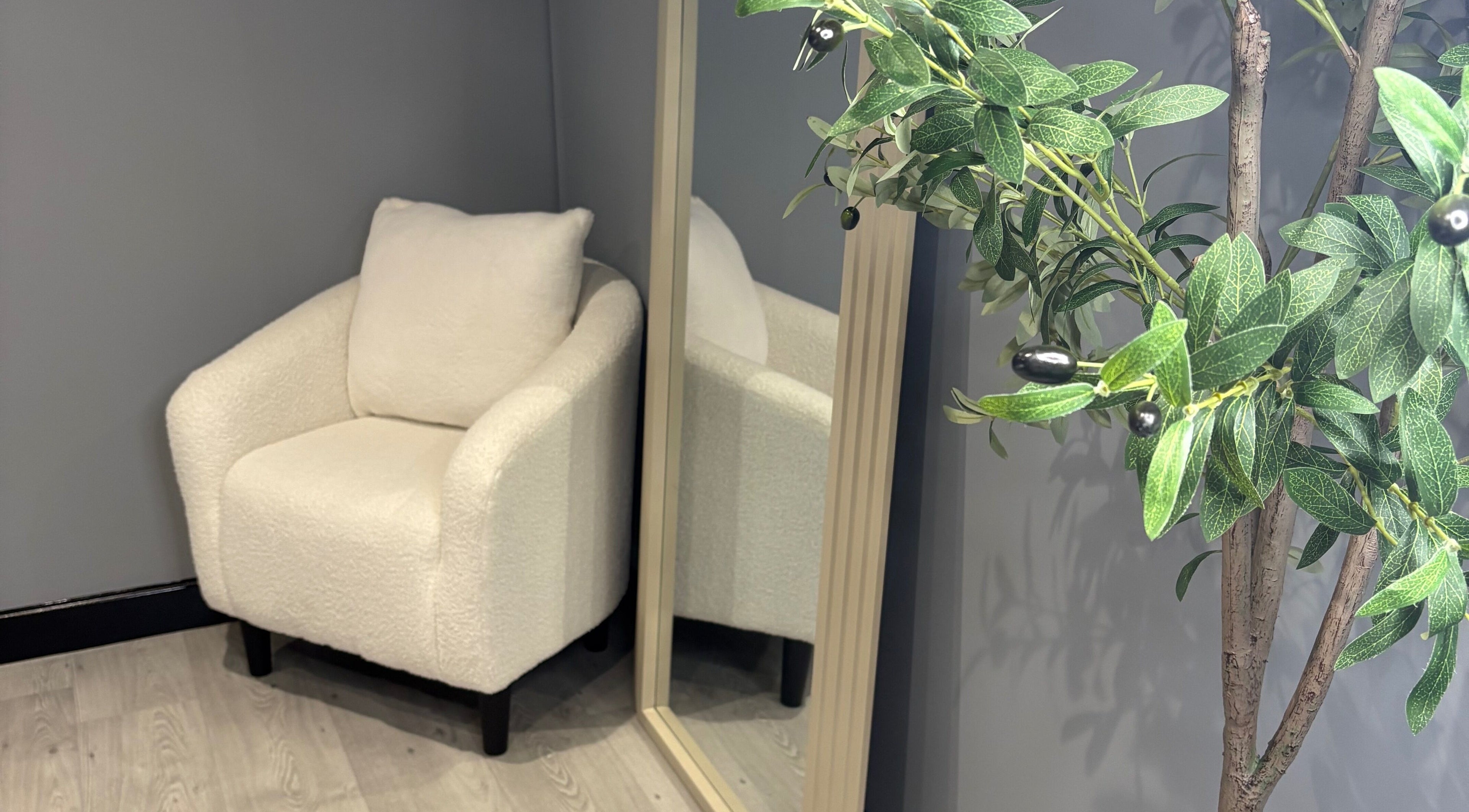 Elegant corner at All About Aesthetics, Fareham, England, GB with white chair, mirror, and plant.