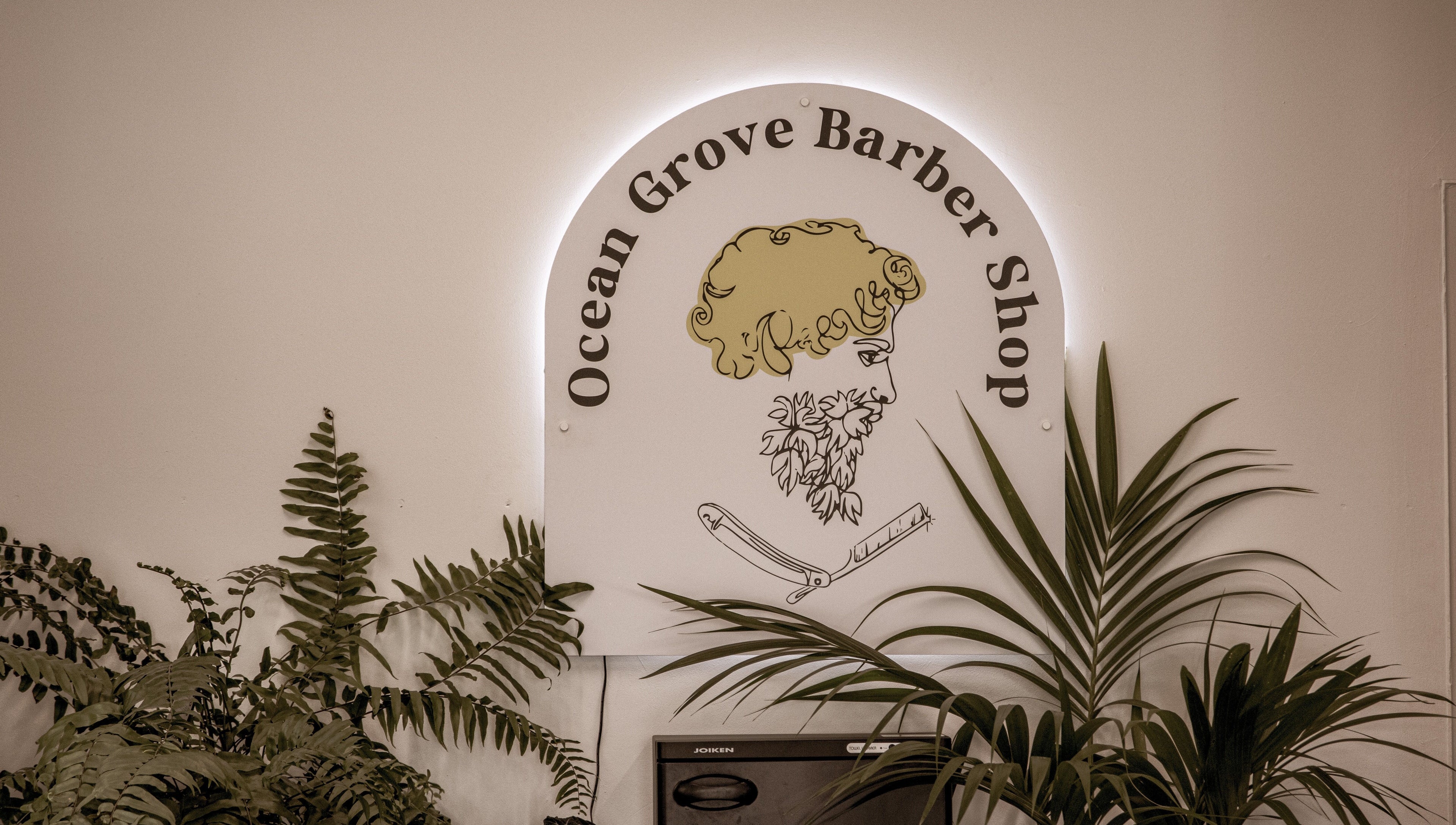 Ocean Grove Barbershop logo surrounded by plants, showcasing modern style in Ocean Grove, VIC, AU.