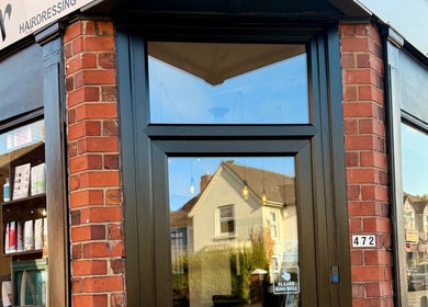 Exterior view of Ivor Hairdressing in Stoke-on-Trent, England, GB with a stylish brick facade and modern glass door.