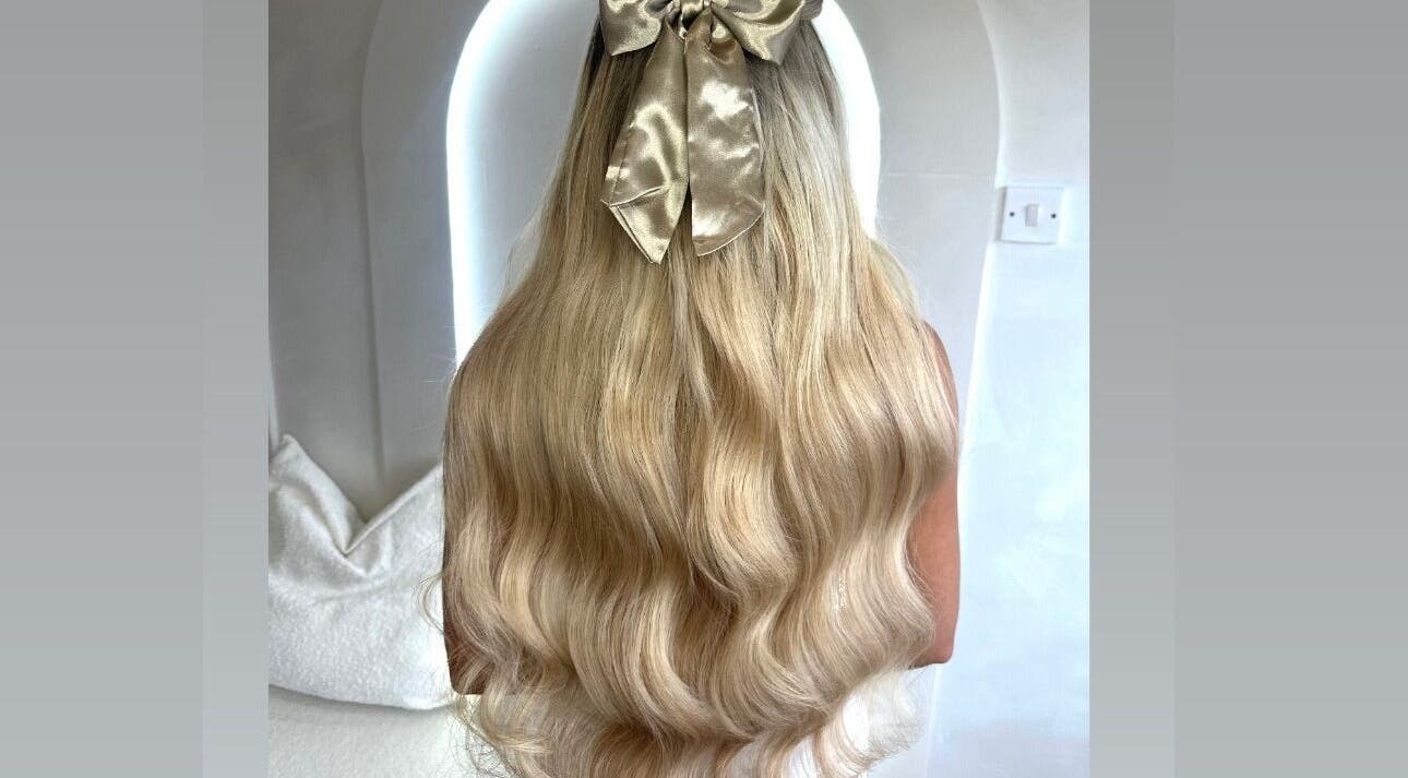 Woman with long, wavy blonde hair and a golden bow at Slae Salon, North Shields, England, GB.