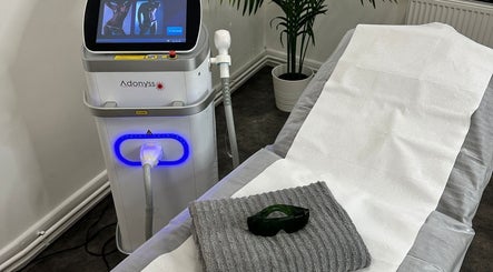 Olga Genc Beauty in Chichester, England, showcases a modern laser treatment setup with equipment and relaxation bed.
