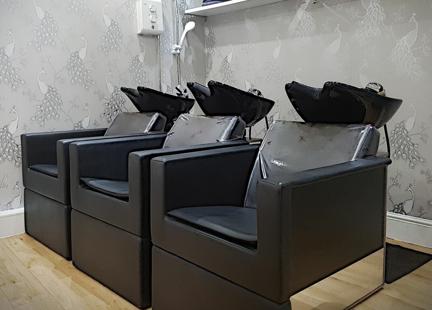 Stylish hair wash stations at Halo, Congleton, England, GB with sleek black chairs and peacock wallpaper.