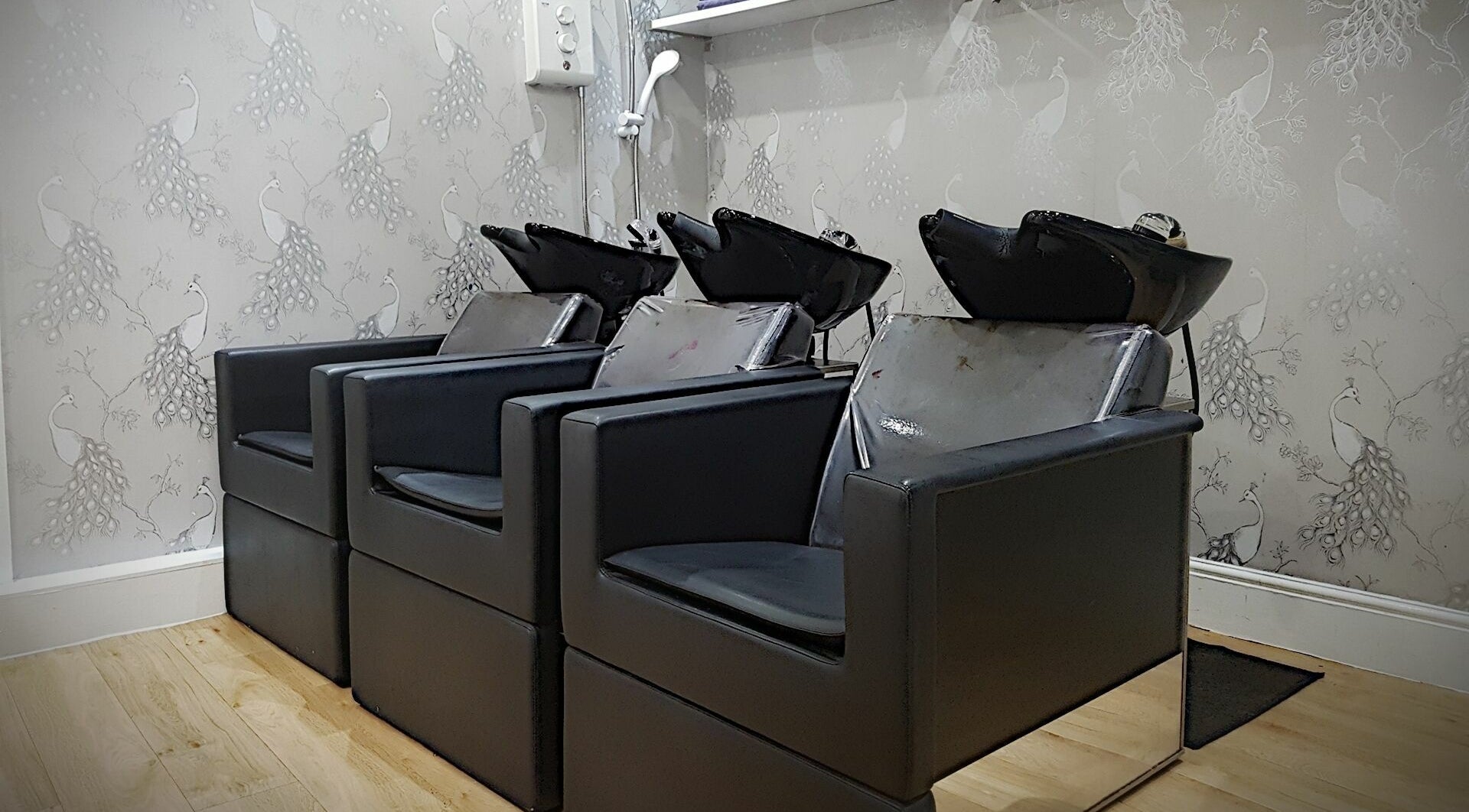 Stylish hair wash stations at Halo, Congleton, England, GB with sleek black chairs and peacock wallpaper.