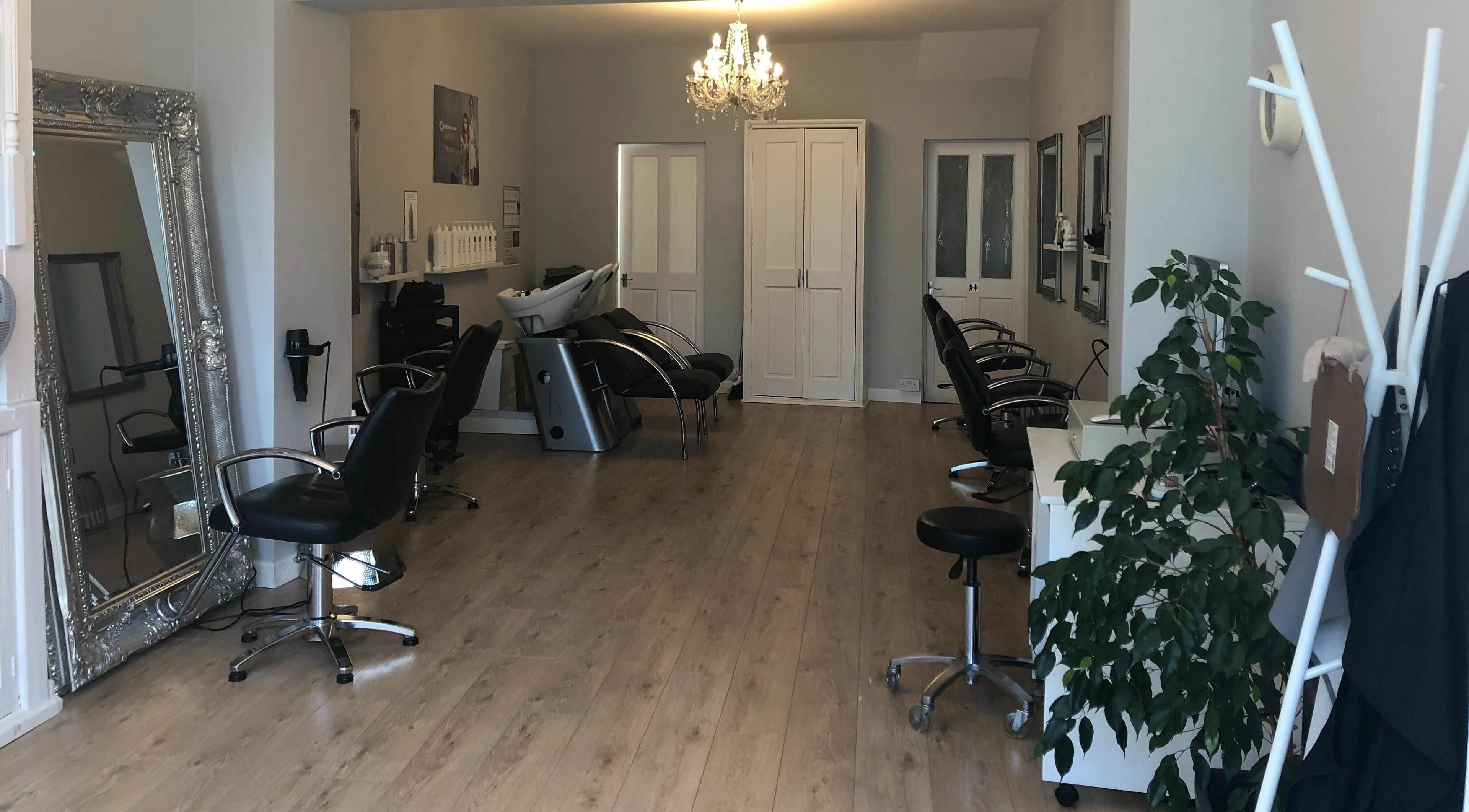 Elegant salon at Eclipz, Woburn Sands, England, GB with stylish chairs and a lavish mirror under a chandelier.
