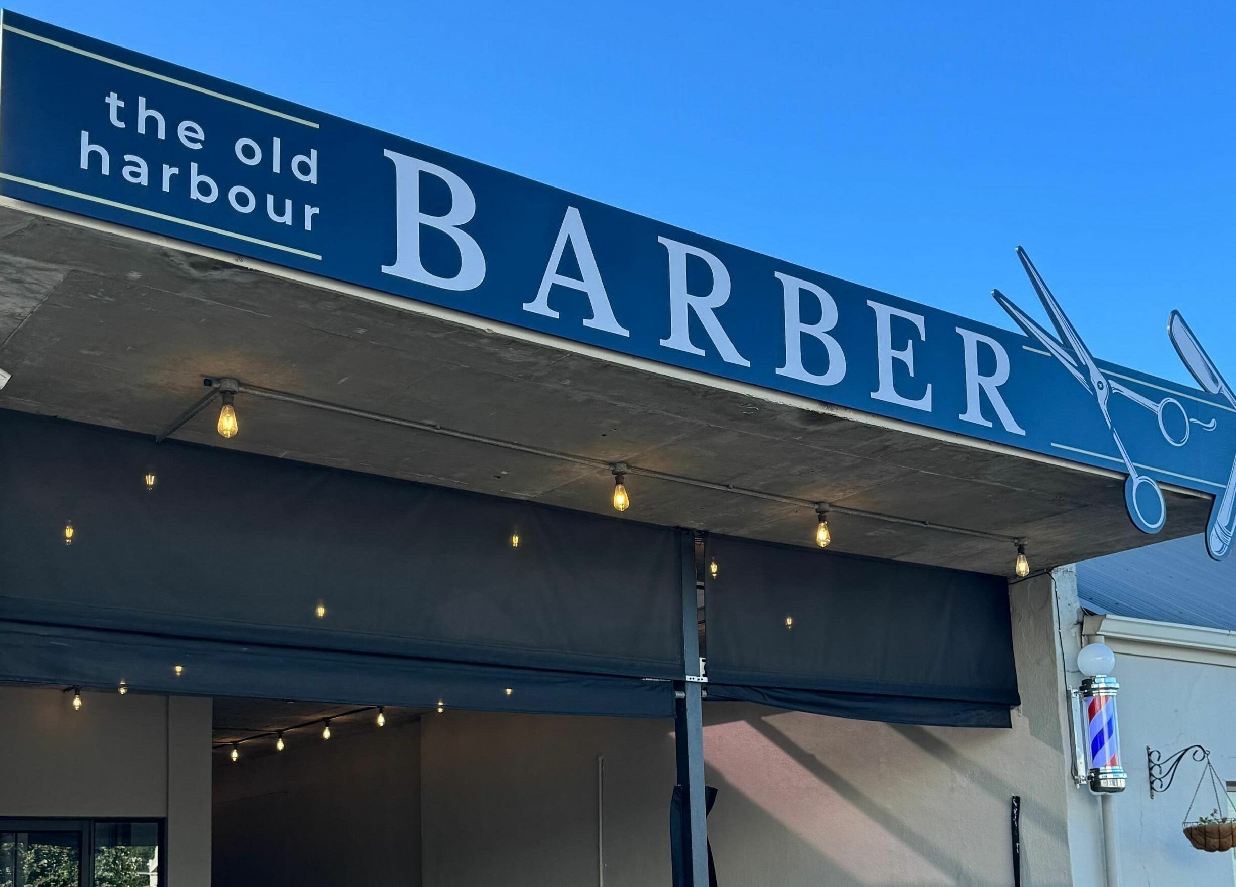 Exterior of The Old Harbour Barber in Hermanus, Western Cape, ZA with stylish sign and classic barber pole.