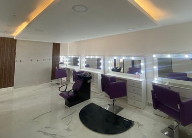 Sala de belleza elegante en Lesslie Beauty, Monterrey, Nuevo León, MX, con sillas moradas y espejos iluminados.