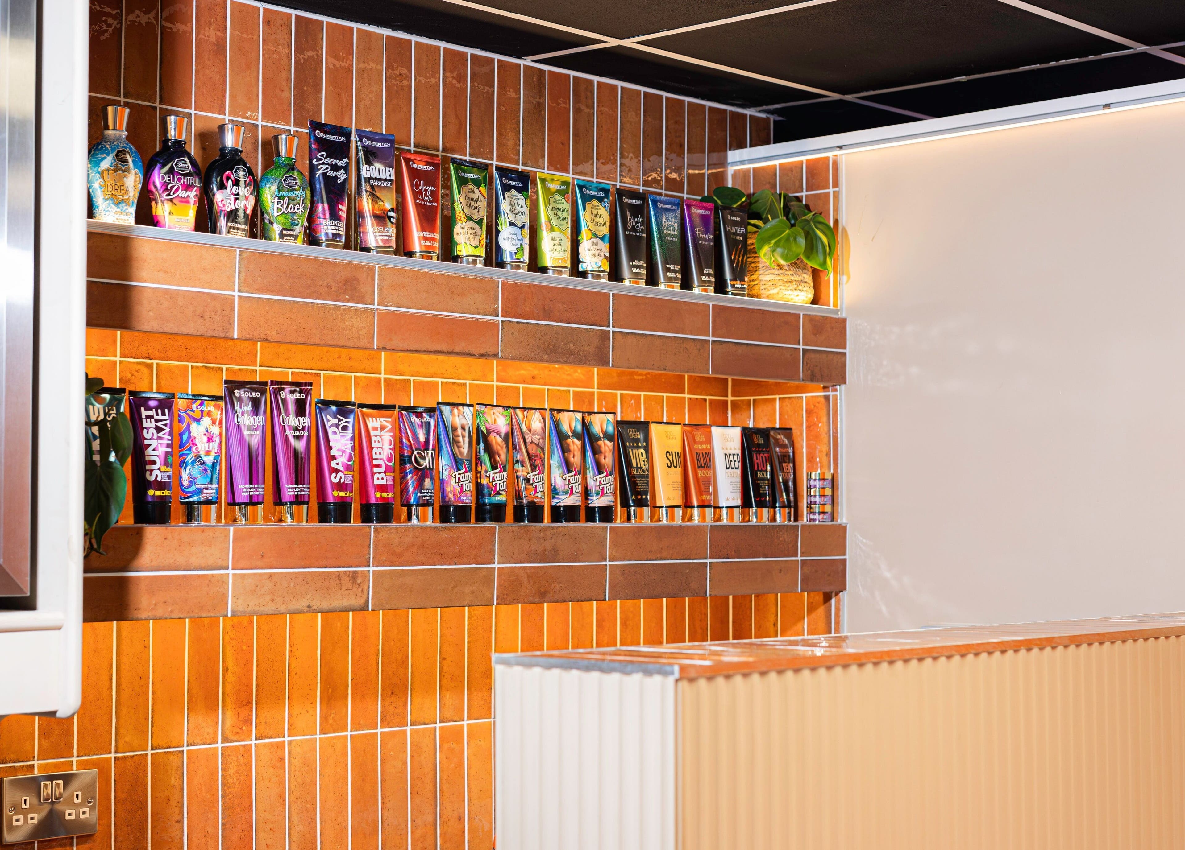 Shelf of tanning lotions at Glow Club, Skegness, GB. Bright orange-tiled backdrop enhances the colorful products.