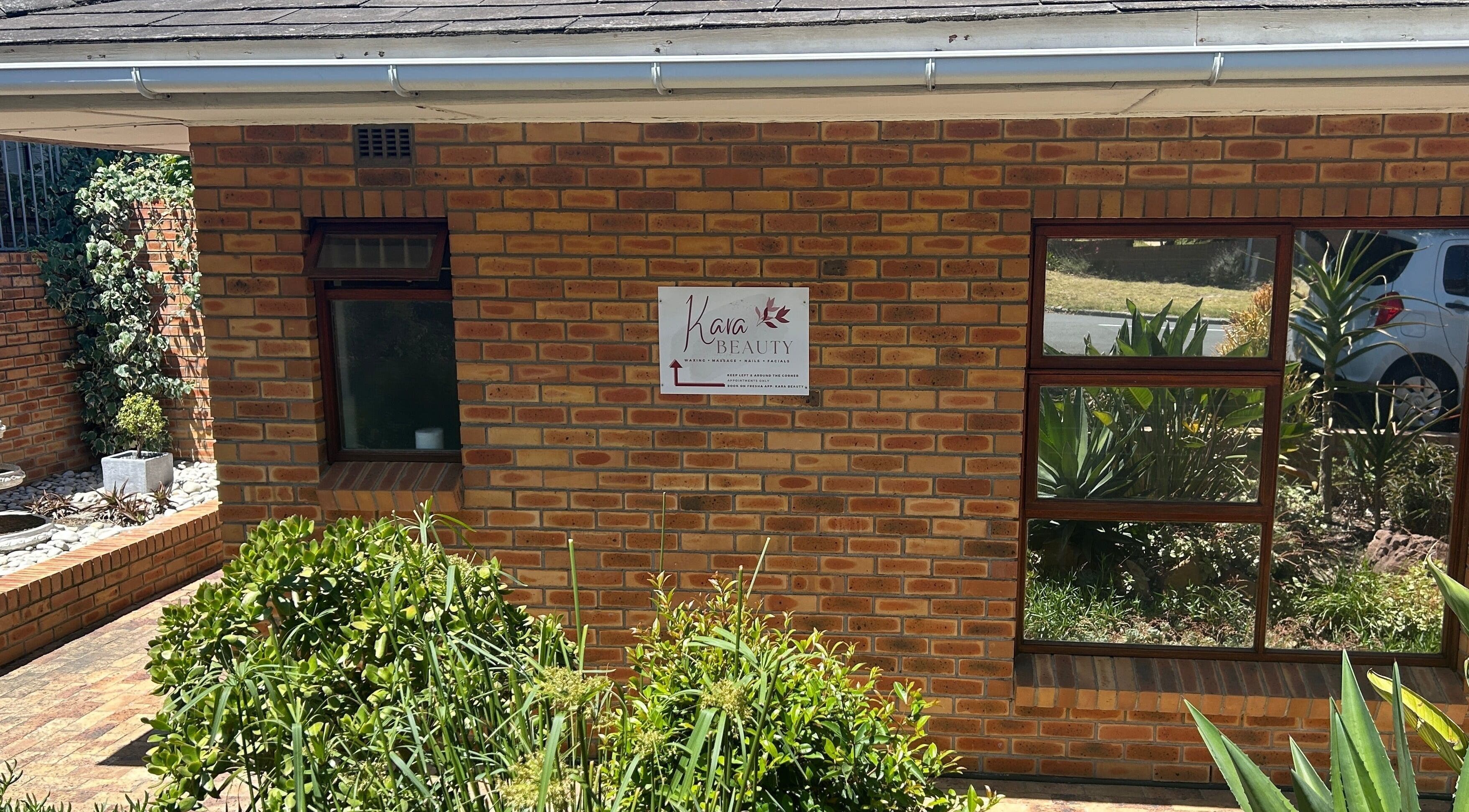 Front view of Kara Beauty in Cape Town, Western Cape, ZA, showcasing brick exterior and lush plants.