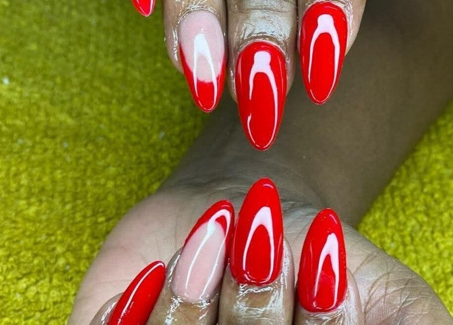 Red acrylic nails beautifully polished at Nenebeauty Bar, Centurion, Gauteng, ZA on a vibrant green background.