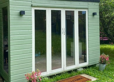 Cozy garden room at Izzy’s Beauty Room, Gloucester, England, GB, featuring glass doors and greenery.