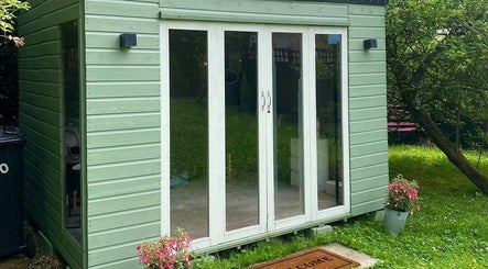 Cozy garden room at Izzy’s Beauty Room, Gloucester, England, GB, featuring glass doors and greenery.