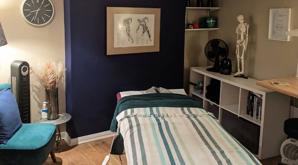 Therapy room at Reviving Harmony, London showing massage table, decor, and anatomy art. Booking info via email.