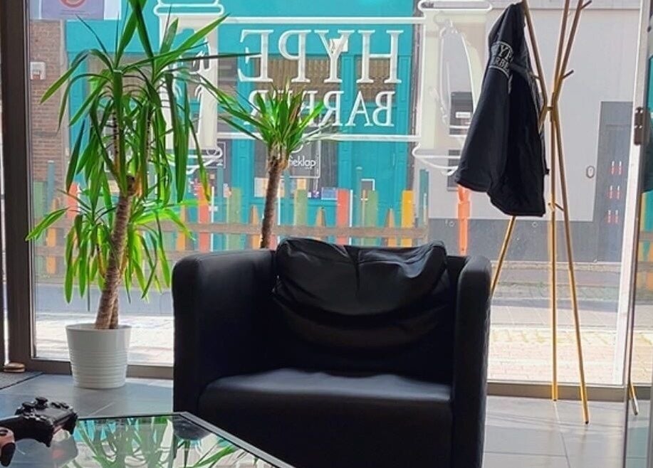 Stijlvolle zithoek bij HYPE BARBERSHOP in Antwerpen, Vlaams Gewest, BE met een moderne fauteuil en planten.