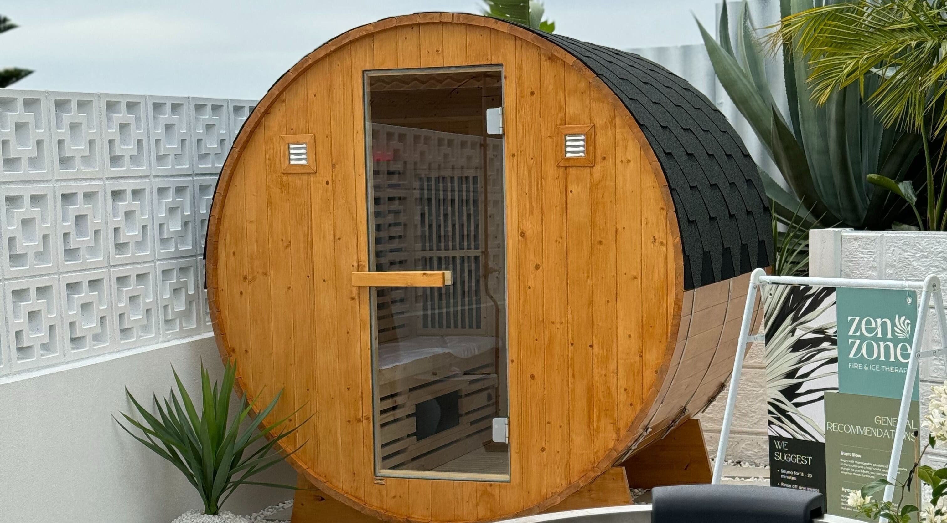 Wooden barrel sauna at Zen Zone Perth, Beldon, Western Australia, AU, surrounded by lush plants.