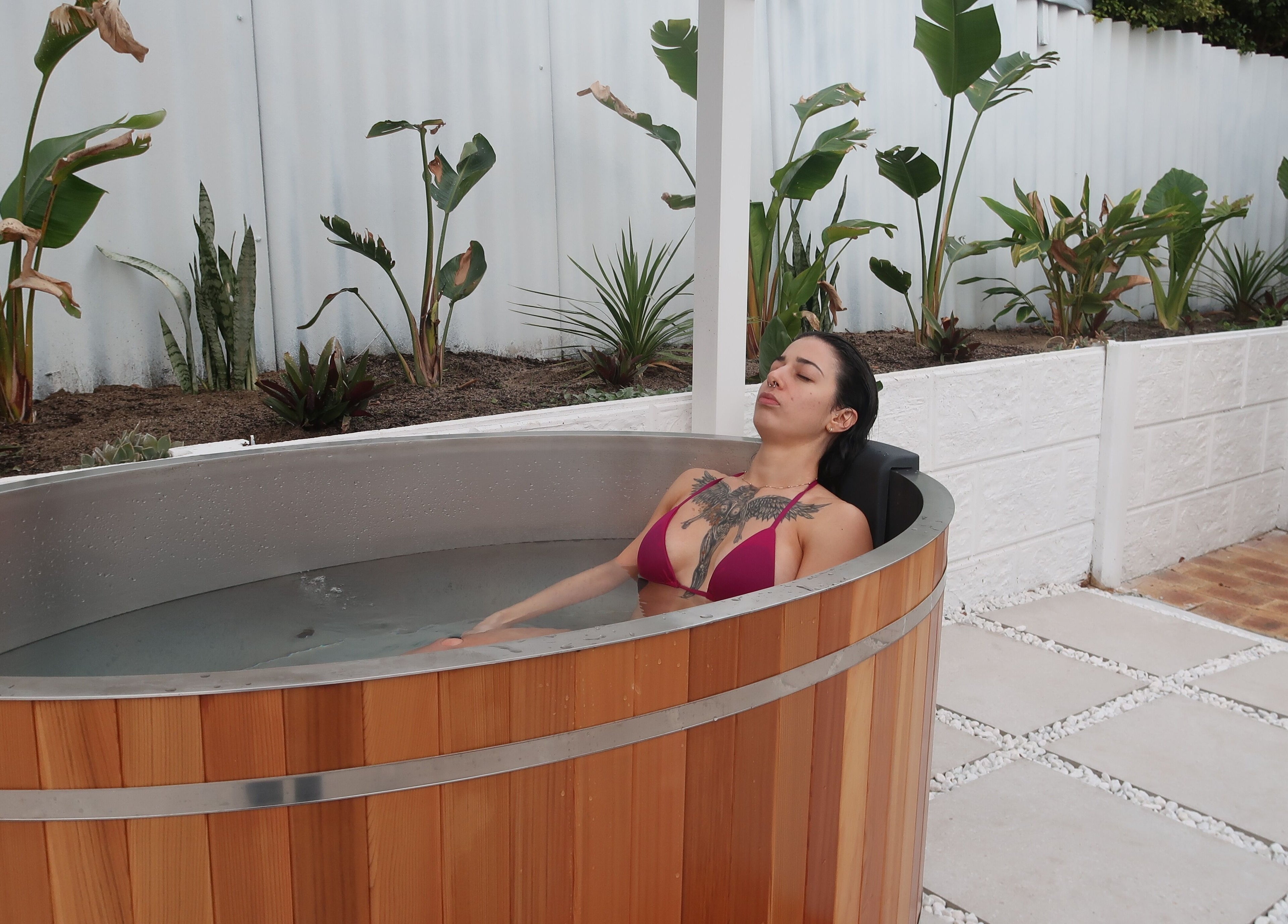 A person relaxes in a wooden spa tub at Zen Zone Perth in Beldon, Western Australia, AU with lush greenery.