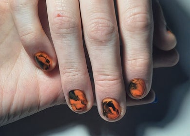 Original diseño de uñas en Purple Paw Nails, Santiago, Región Metropolitana, CL, destacando tonos anaranjados y negros.