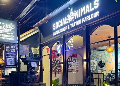 Front of Social Animals Barbershop & Tattoo Parlour in Canggu, Bali, ID, at night with vibrant signage.