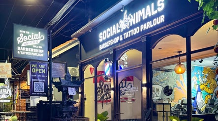 Front of Social Animals Barbershop & Tattoo Parlour in Canggu, Bali, ID, at night with vibrant signage.