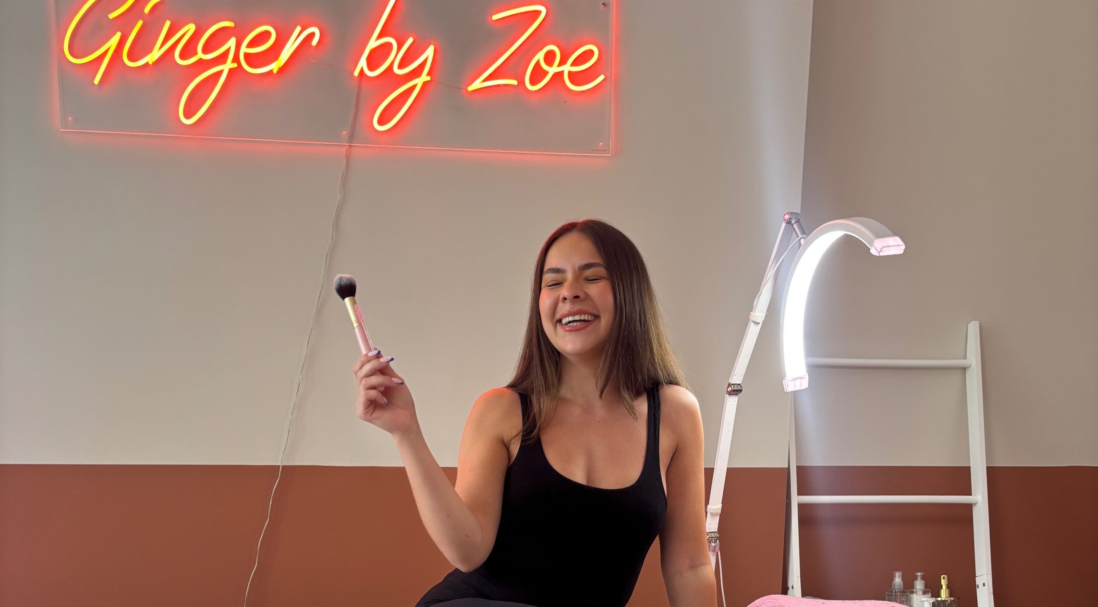 Smiling woman holds makeup brush at Face by Caitlyn in Ginger by Zoe, Cardiff, Wales, GB.