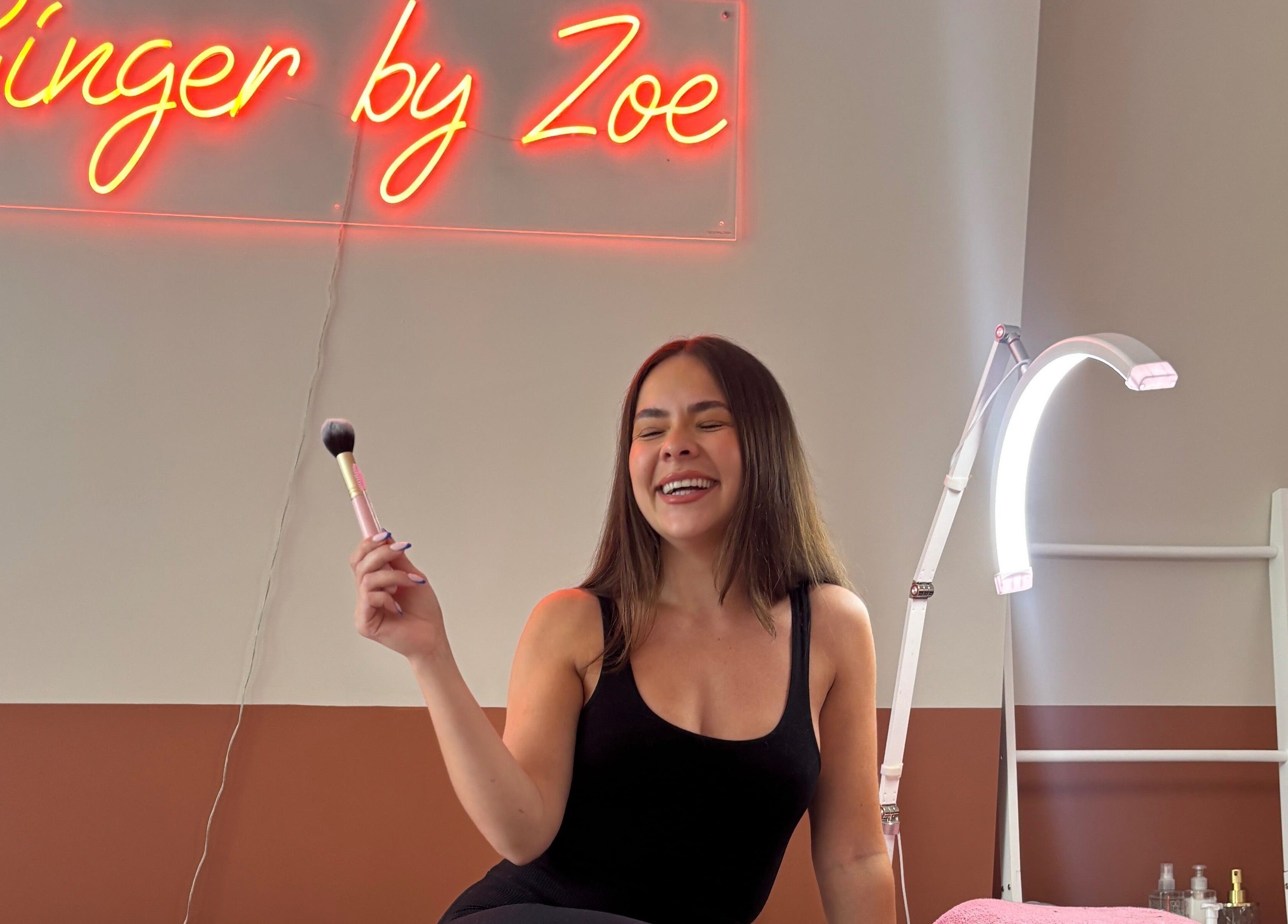 Woman smiling with beauty tool at Face by Caitlyn in Ginger by Zoe, Cardiff, Wales, GB under neon sign.