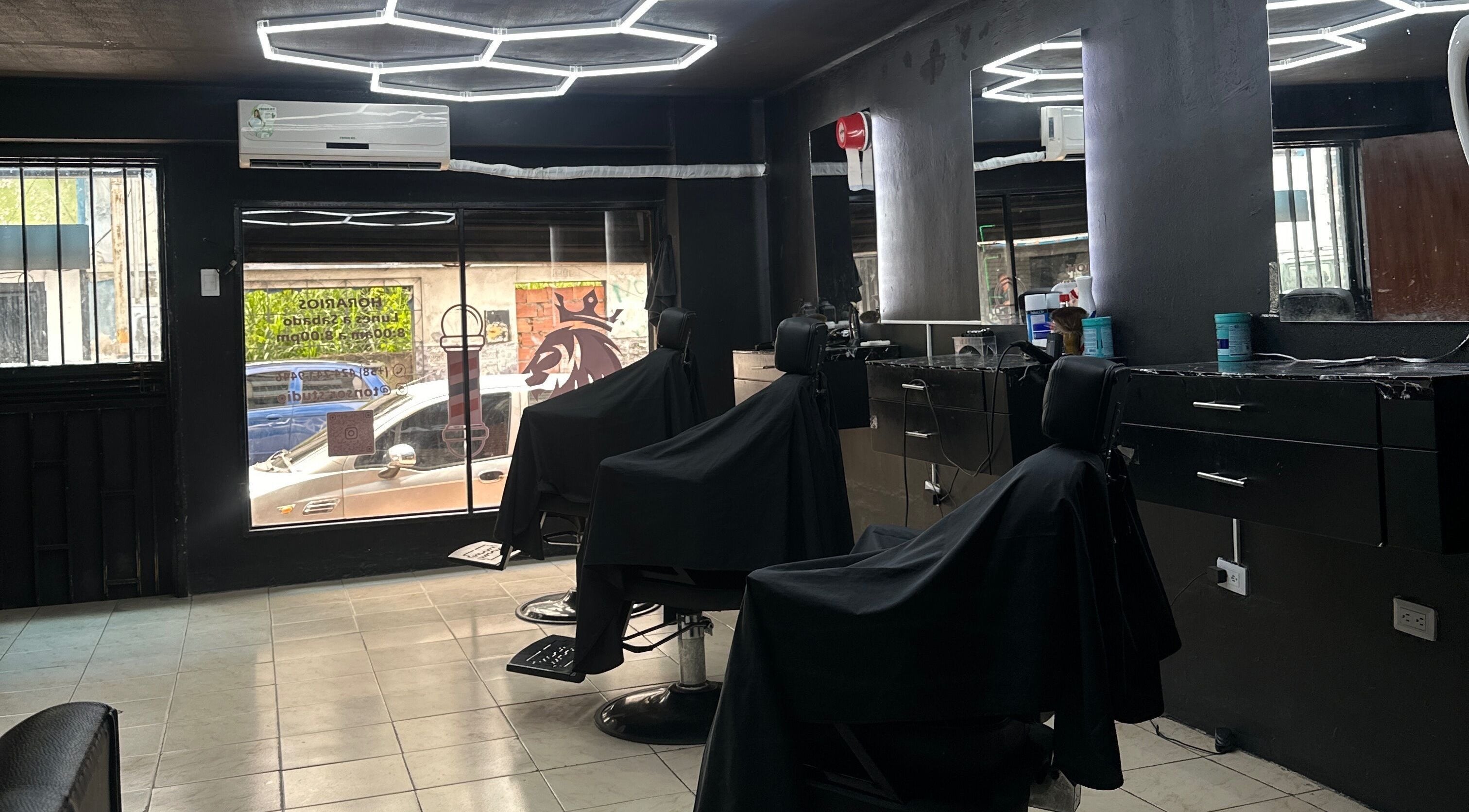 Interior de Tonsor Studio en San Cristóbal, Táchira, VE con sillas negras y estantes elegantes.