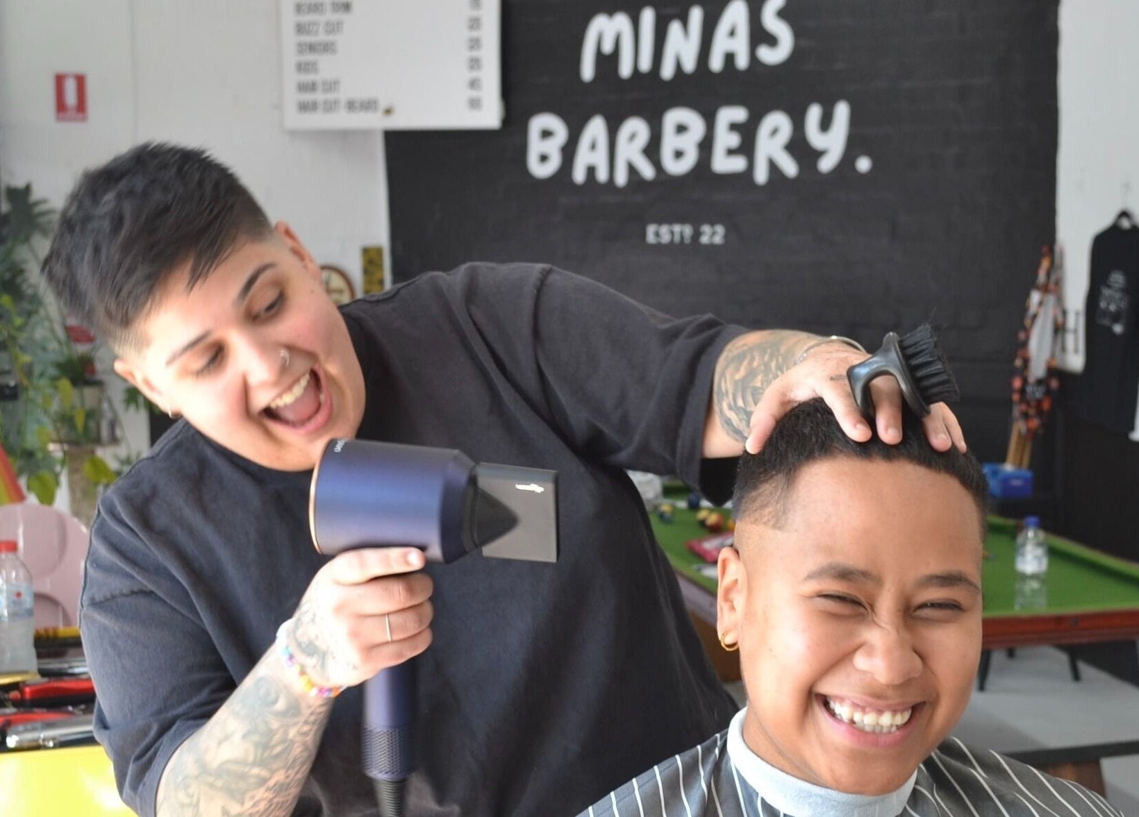 Barber at Minas Barbery in Enmore, NSW, AU gives a smiling client a stylish haircut.