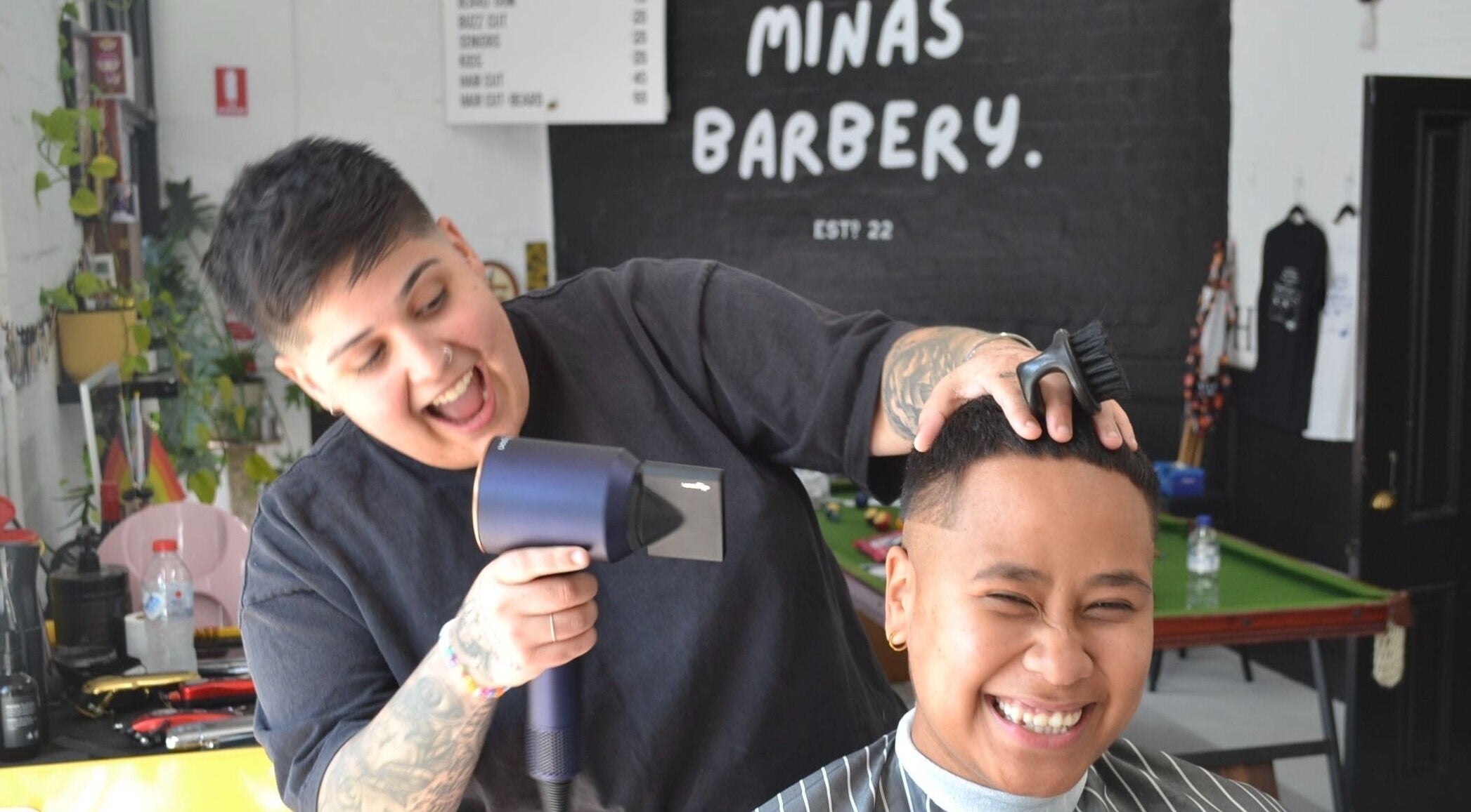Barber at Minas Barbery in Enmore, NSW, AU gives a smiling client a stylish haircut.