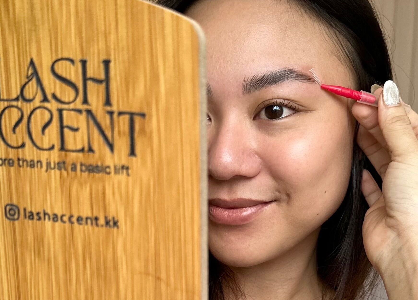 A smiling woman uses a lash tool in front of a Lash Accent mirror in Kota Kinabalu, Sabah, MY.