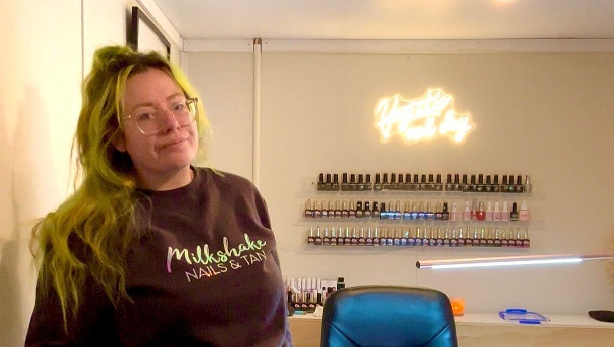 A welcoming staff member at Milkshake Nails & Tan in Waitara, Taranaki, NZ, with a display of nail polishes.