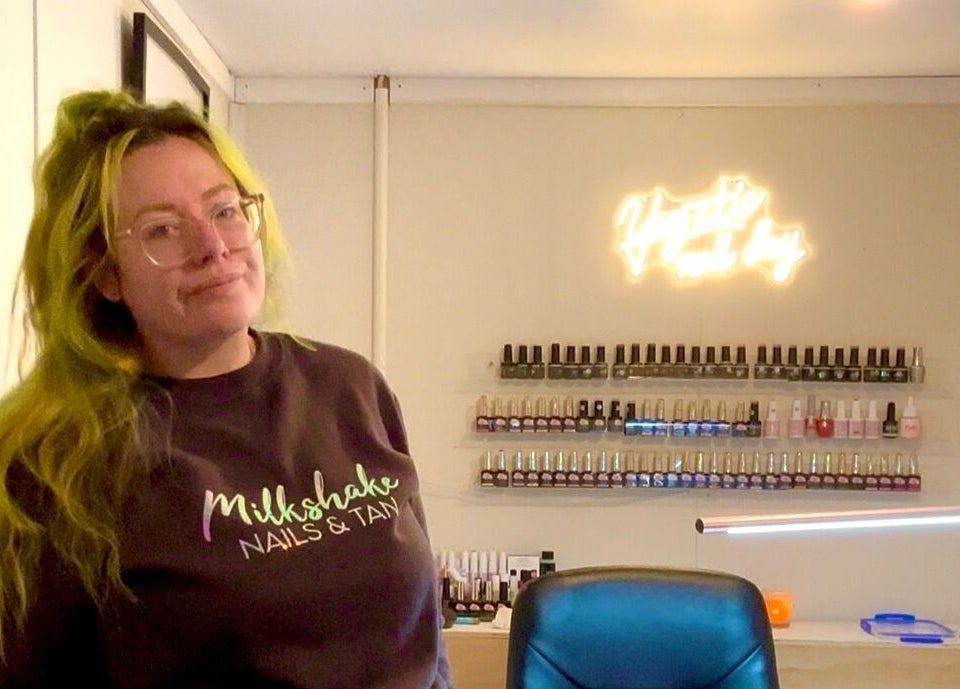 A welcoming staff member at Milkshake Nails & Tan in Waitara, Taranaki, NZ, with a display of nail polishes.