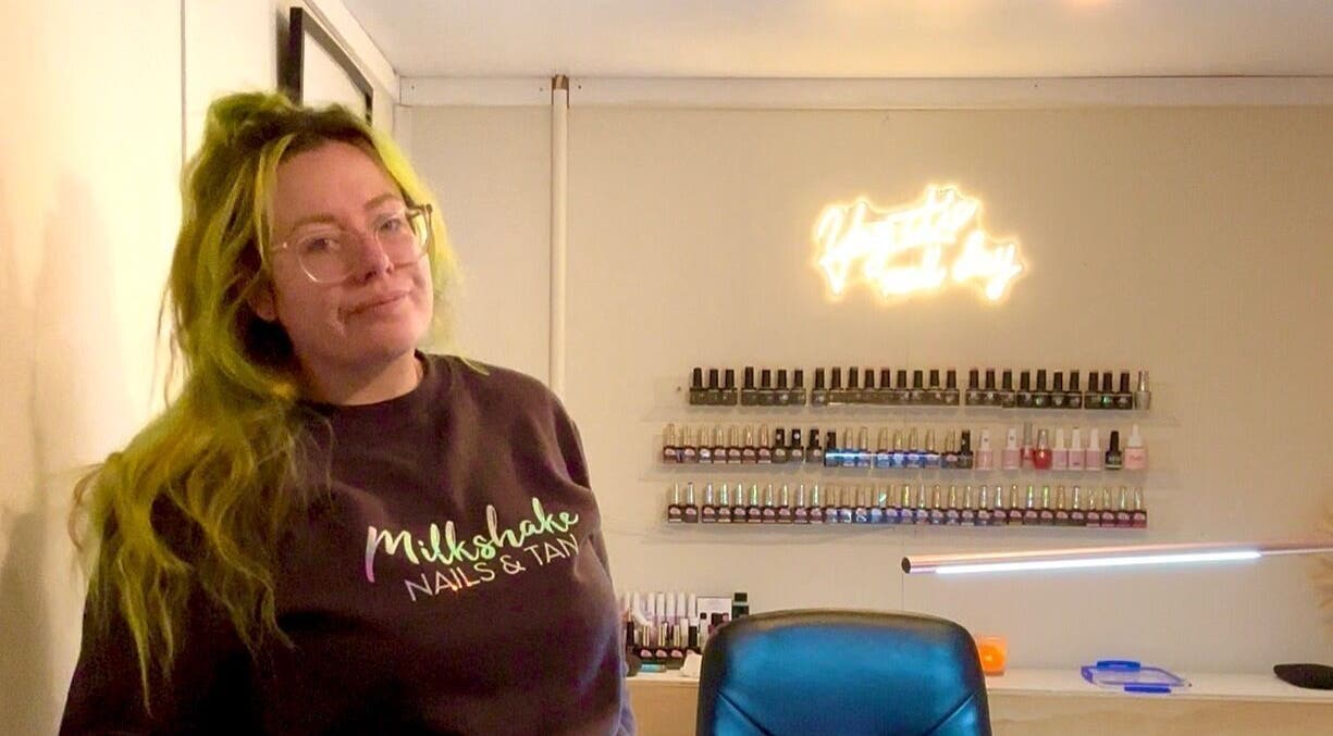 A welcoming staff member at Milkshake Nails & Tan in Waitara, Taranaki, NZ, with a display of nail polishes.