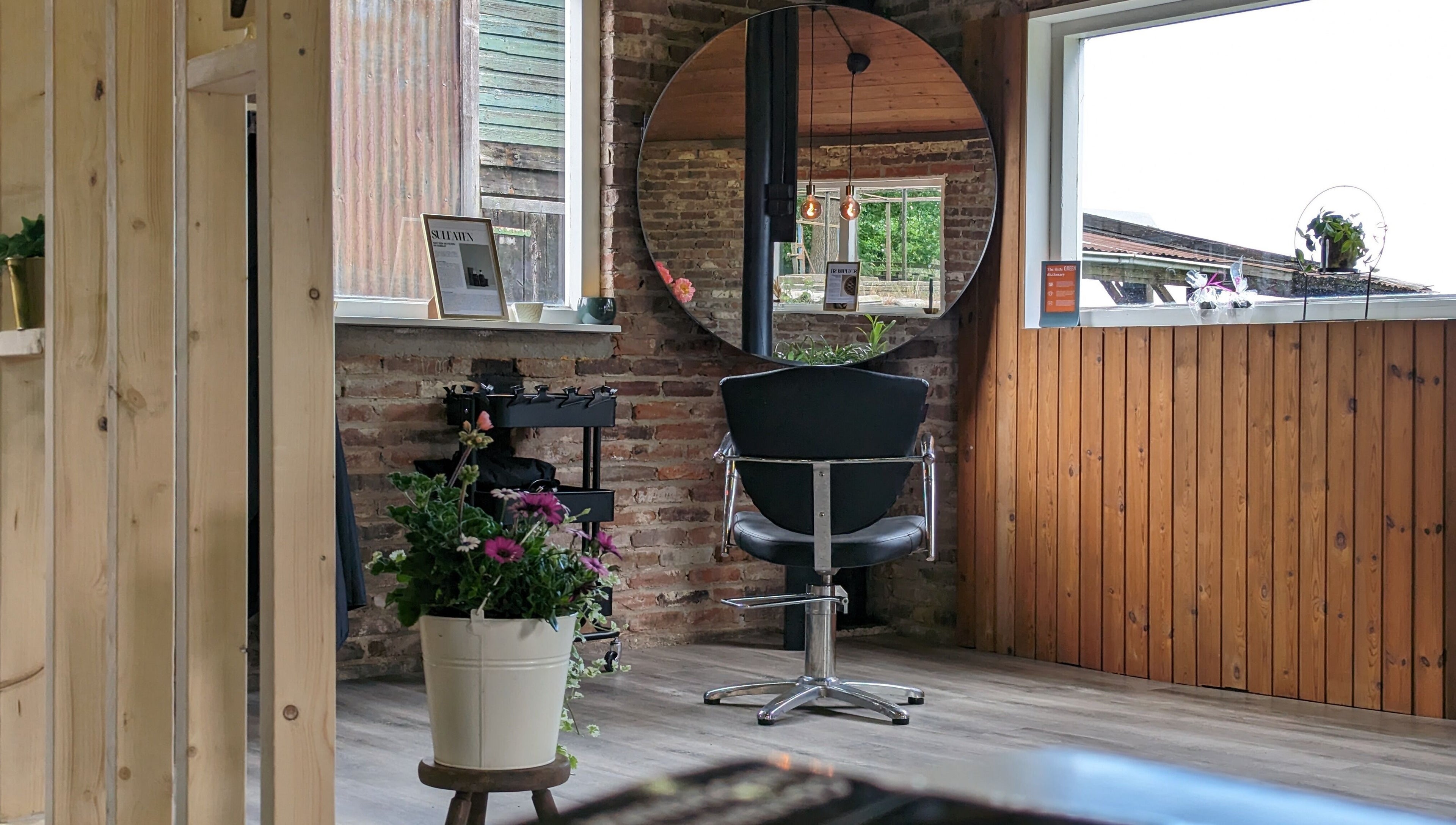 Stijlvolle kapstoel bij Mina Haarsalon in Vroomshoop, Overijssel, NL, met een ronde spiegel en bloemen.