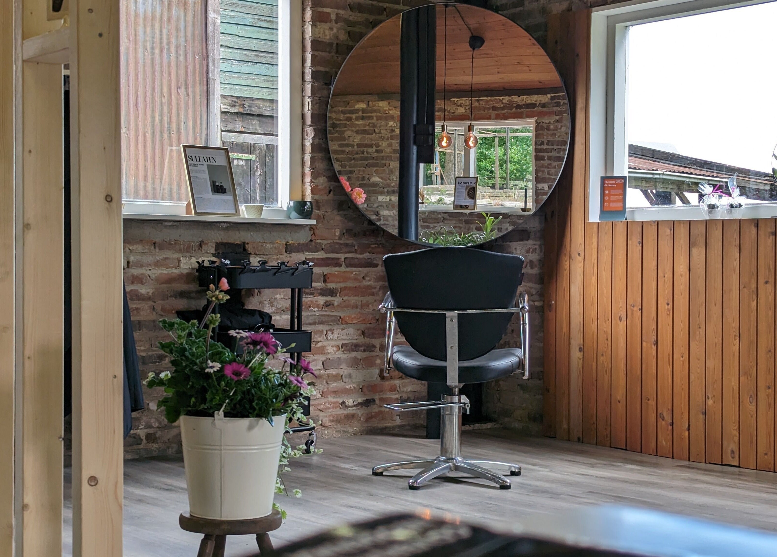 Stijlvolle kapstoel bij Mina Haarsalon in Vroomshoop, Overijssel, NL, met een ronde spiegel en bloemen.