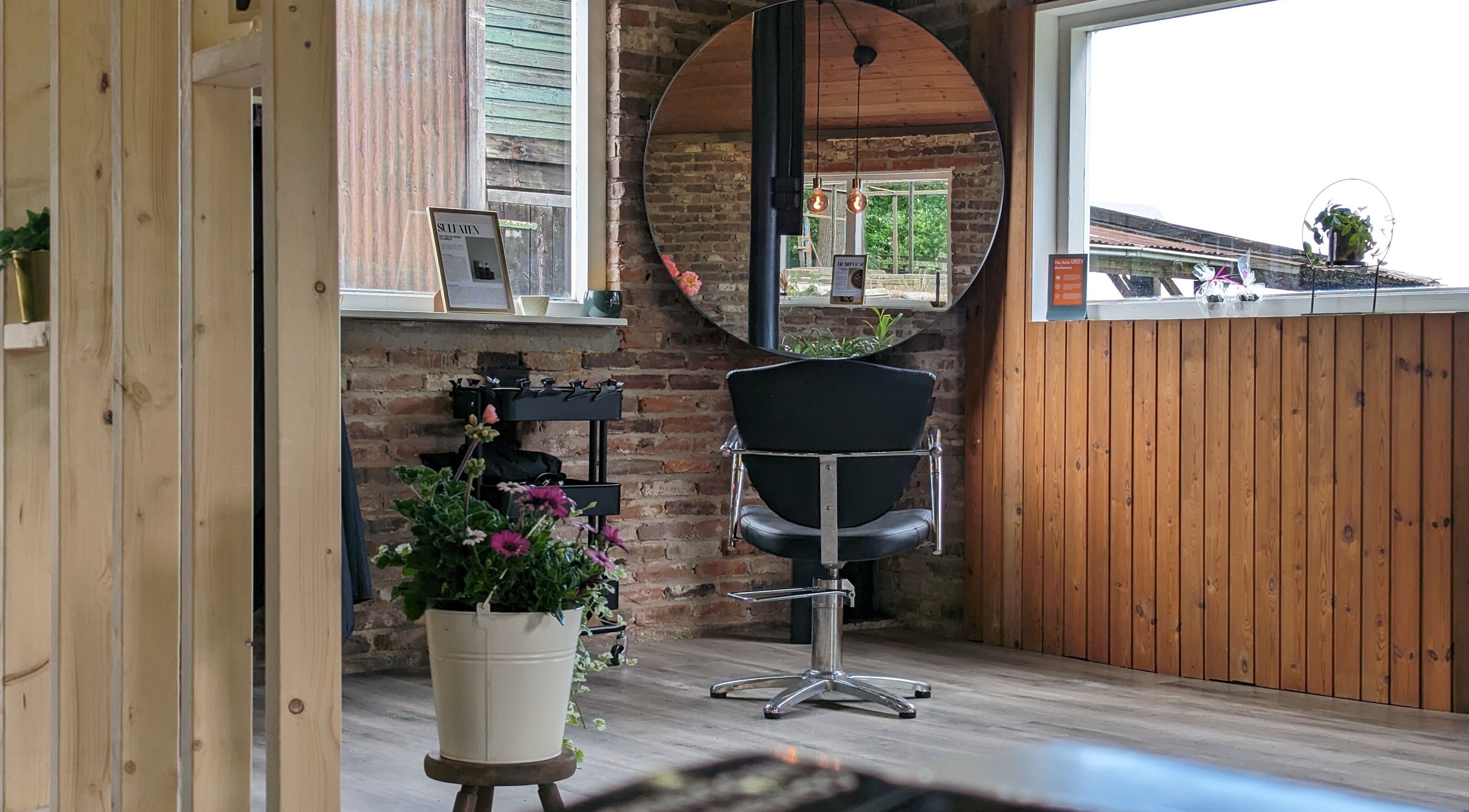 Stijlvolle kapstoel bij Mina Haarsalon in Vroomshoop, Overijssel, NL, met een ronde spiegel en bloemen.