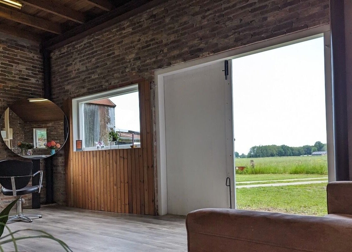 Binnenkant van Mina Haarsalon in Vroomshoop, Overijssel met rustieke bakstenen muur en uitzicht op het landschap.