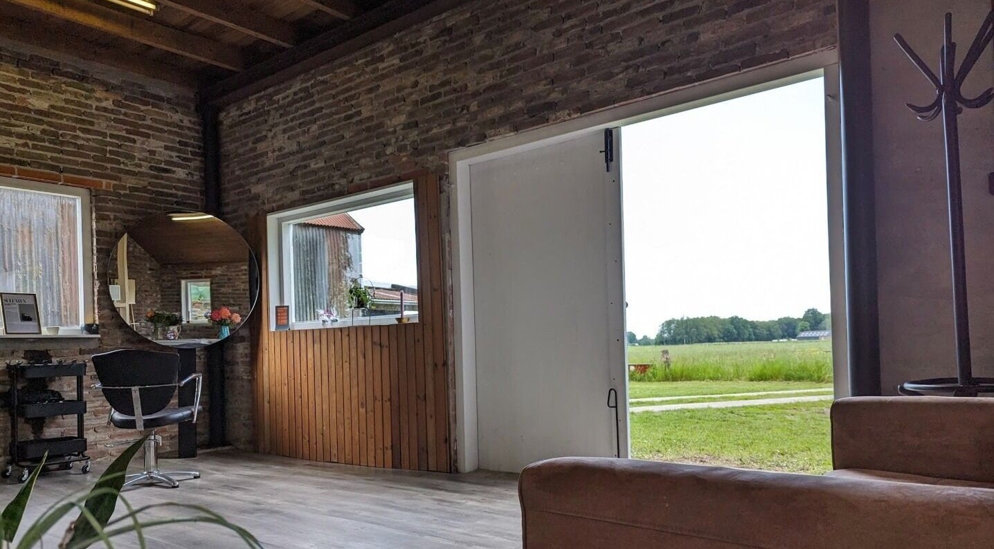 Binnenkant van Mina Haarsalon in Vroomshoop, Overijssel met rustieke bakstenen muur en uitzicht op het landschap.
