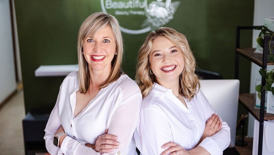 Friendly staff at Perfectly Beautiful, Bloemfontein, Free State, ZA, smiling in white shirts against a green wall.