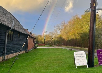 A rainbow arches over The Ivy Rooms, Dunmow, England, GB, against a backdrop of lush greenery and serene sky.