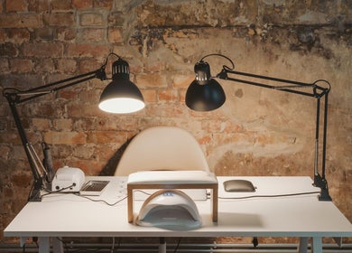 Sleek manicure station at Grieze, Rīga, LV, featuring modern lamps and tools against a rustic brick wall.