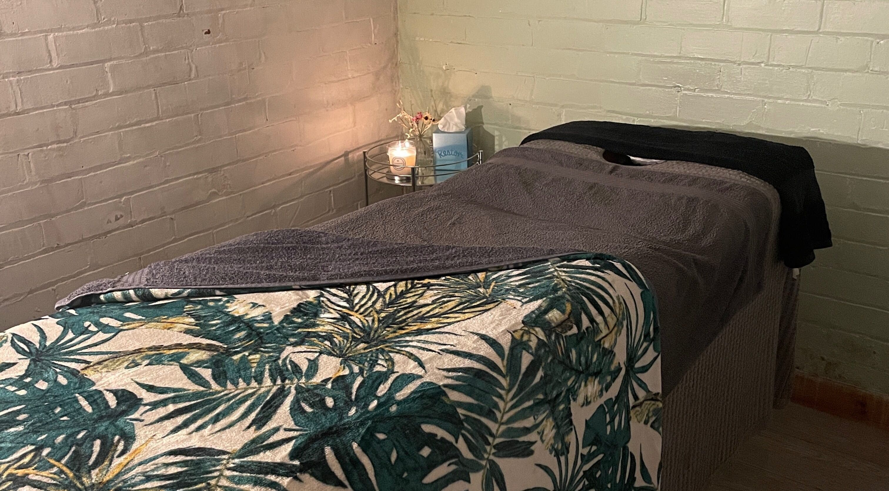 Tranquil massage bed at SW Sports Massage, Wirral, England, GB, with soft lighting and tropical blanket.