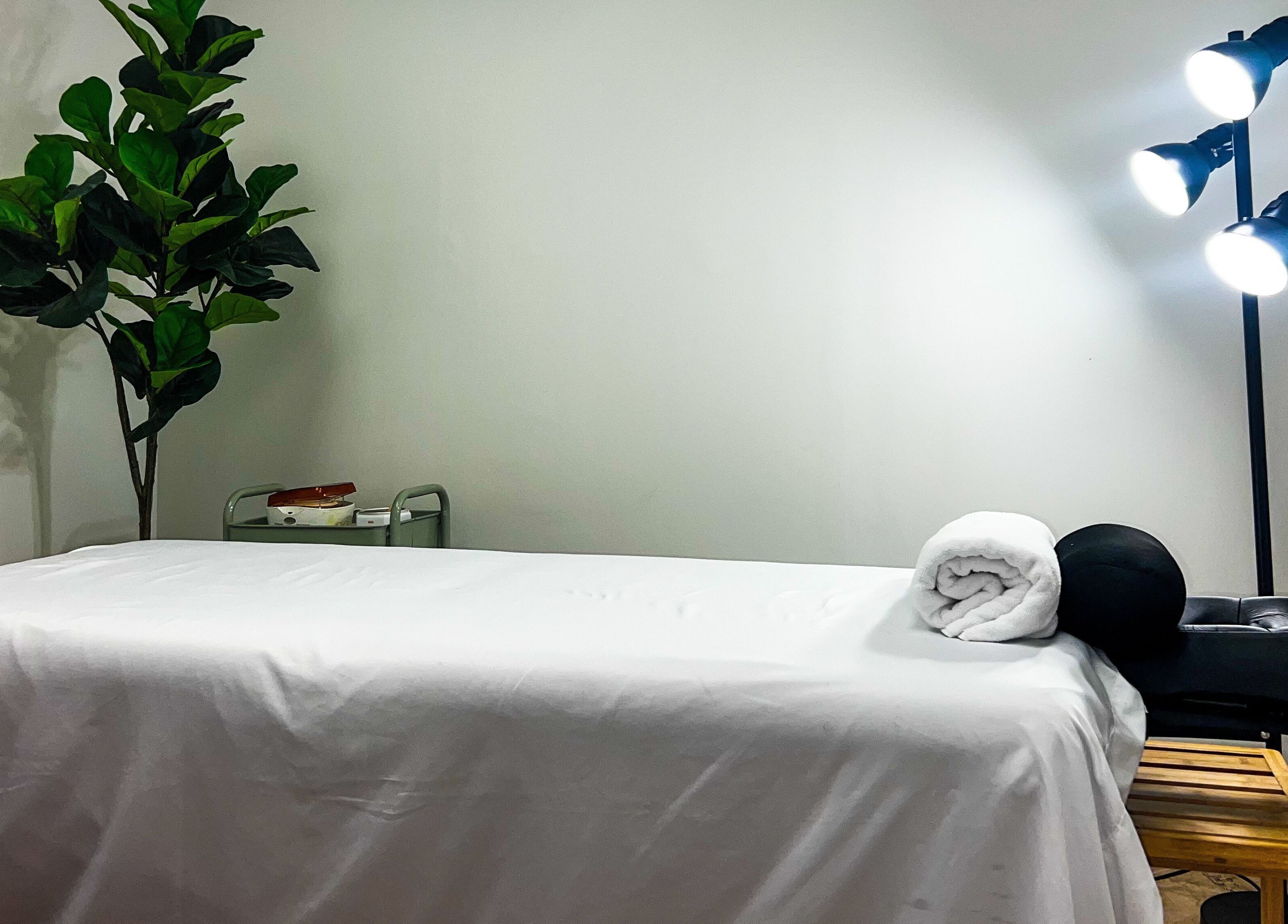 Massage room at My KandA Nail Salon in Grand Cayman, KY with a white bed, rolled towel, and leafy plant.