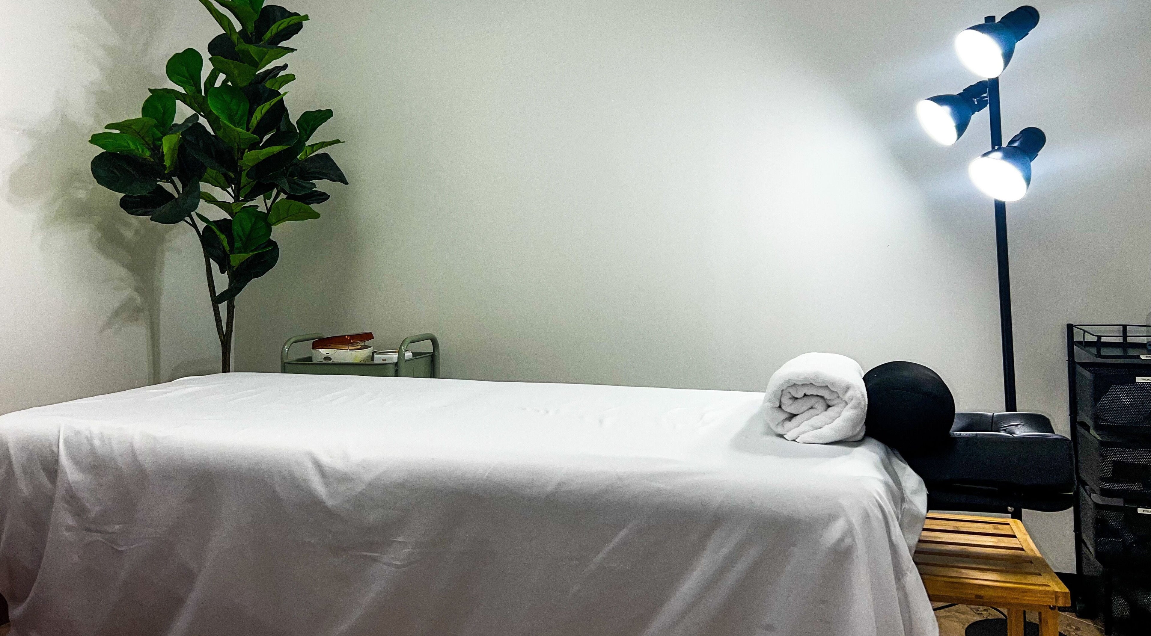 Massage room at My KandA Nail Salon in Grand Cayman, KY with a white bed, rolled towel, and leafy plant.