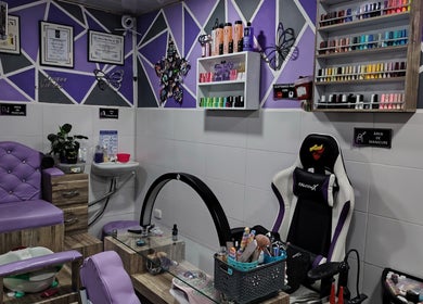 Zona de manicura moderna en NATINAILS, Bogotá, Bogotá, CO con sillas lilas y estantes de esmaltes coloridos.