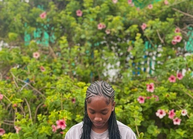 Intricate braided hairstyle at SlayedbyKy, Brighton, St. George, VC, surrounded by vibrant garden backdrop.